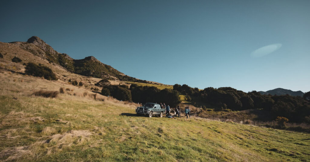 view of Living Springs hills. In the foreground there is an old green ute in the middle of a field with people standing around it.