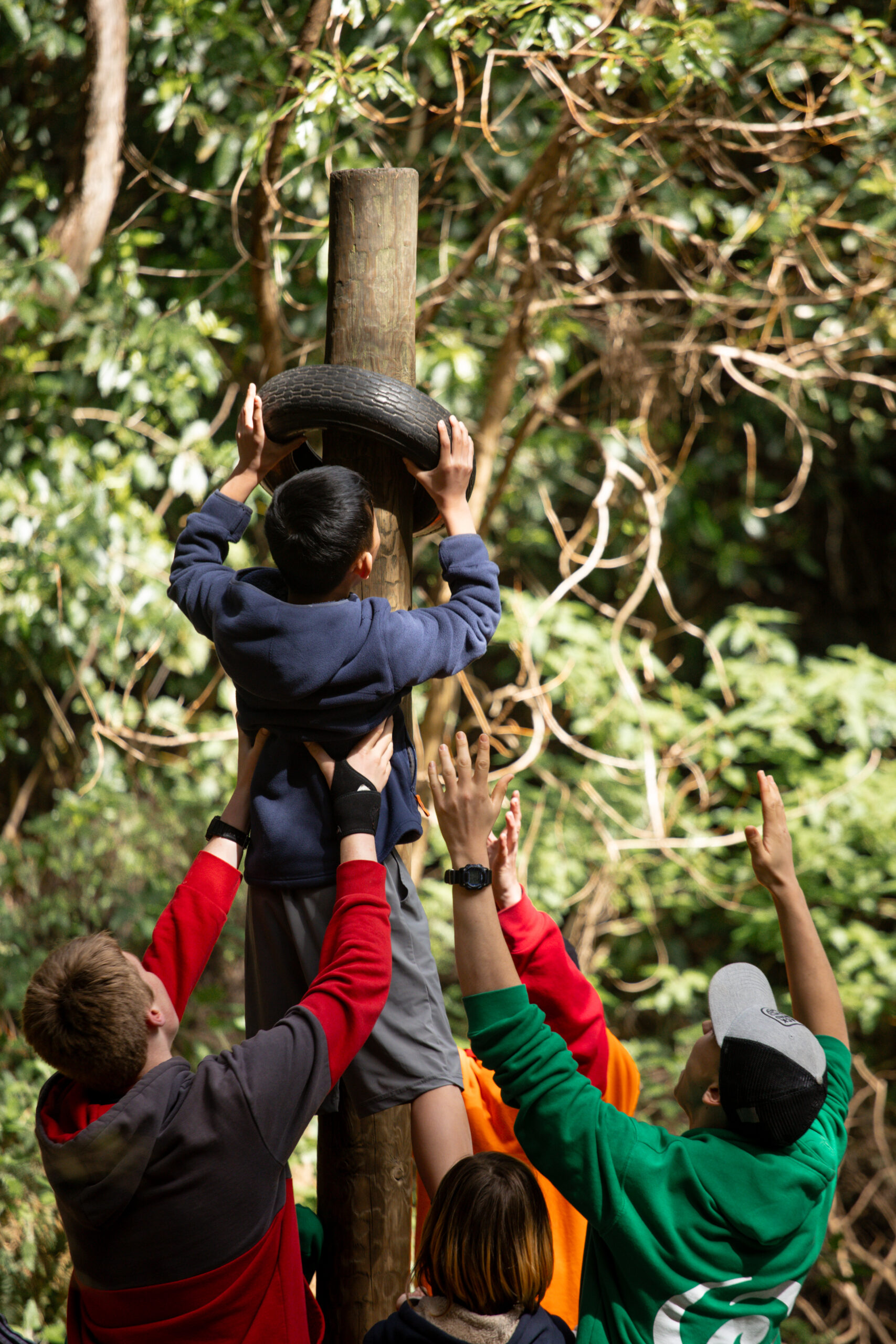 Kids playing in nature, working together to fit a tyre over a pole.